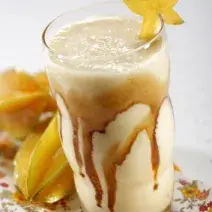 foto tirada de um copo transparente com bebida de carambola e sorvete com calda de caramelo. Ao fundo carambolas.
