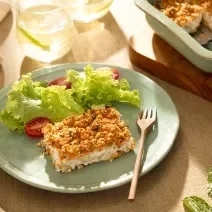 Foto da receita de quibe de abóbora de aveia servida com salada de alface e tomate sobre um pratinho azul com um garfo de madeira ao lado e ao fundo há uma forma com o restante do quibe