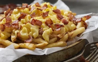 Fotografia de uma porção de batatas fritas cobertas por queijo cheddar e pedaços de bacon. Fotografia de uma porção de batatas fritas cobertas por queijo cheddar e pedaços de bacon.