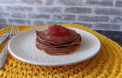 Imagem Imagem da receita de Panqueca Americana nutritiva com cobertura de geleia de frutas, em um prato branco, e ao lado os talheres Imagem Imagem da receita de Panqueca Americana nutritiva com cobertura de geleia de frutas, em um prato branco, e ao lado os talheres