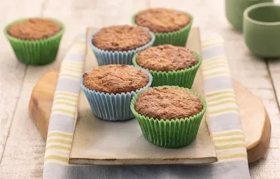 Foto da Receita de Cupcake Leve FiberMais. Observa-se uma tábua de madeira sobre um guardanapo listrado e os cupcakes em cima em forminhas verdes e azuis.