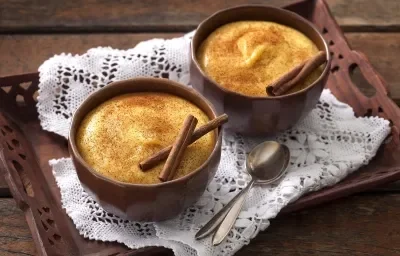 Foto de uma bandeja marrom com uma toalha branca em cima e 2 potes marrons com curau dentro e canela decorando Foto de uma bandeja marrom com uma toalha branca em cima e 2 potes marrons com curau dentro e canela decorando