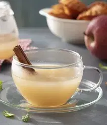 Imagem de uma xícara transparente de chá de maçã com um pedaço de canela em pau