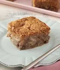 Foto de uma fatia de bolo de banana sobre um prato branco com um garfo do lado direito