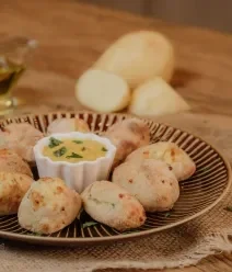 Recriando com a Air Fryer: Reaproveite a Ceia! Fotografia de um prato raso escuro com croquetes de batata em volta de um pote branco com molho.