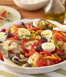 Fotografia mostra um prato de servir branco com bacalhau, pimentão, ovo e azeitona preta. Fotografia mostra um prato de servir branco com bacalhau, pimentão, ovo e azeitona preta.