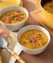 Fotografia mostra duas cumbucas servindo um caldo amarelado com pedaços de bacon e legumes. Fotografia mostra duas cumbucas servindo um caldo amarelado com pedaços de bacon e legumes.
