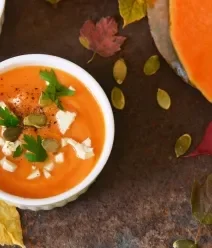 MATERNA: Receitas para Fortalecer a Sua Jornada Foto vista de cima de um recipiente fundo branco com creme de abóbora sobre uma mesa de madeira.