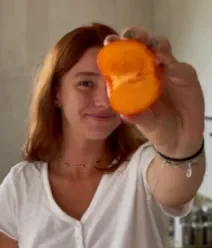 Fotografia mostra uma mulher segurando um pessego na mão, cobrindo metade do seu rosto.
