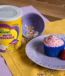 Receitas com Ninho Nutri Advance Foto de um cupcake com cobertura rosa em um prato com morango ao lado da lata de NINHO Nutri Advance.