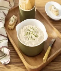 Imagem de um pote branco ao meio com patê de atum dentro e ao lado espátula e pedaços de pães