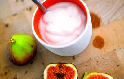 Fotografia de um creme de figo com creme de leite em um recipiente de cerâmica na cor branco e vermelho. Ao redor, dois figos inteiros e mais duas metades do fruto ao lado. Fotografia de um creme de figo com creme de leite em um recipiente de cerâmica na cor branco e vermelho. Ao redor, dois figos inteiros e mais duas metades do fruto ao lado.