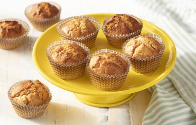 Fotografia em tons de amarelo em uma bancada de madeira branca, um paninho listrado com verde e branco, um prato amarelo alto com vários cupcakes de iogurte com laranja. Fotografia em tons de amarelo em uma bancada de madeira branca, um paninho listrado com verde e branco, um prato amarelo alto com vários cupcakes de iogurte com laranja.