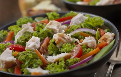 Fotografia em tons de verde, em uma bancada de madeira de cor marrom. Ao centro, um prato redondo preto contendo a salada e ao fundo, um outro prato contendo salada. Ao lado, há um garfo de inox. Fotografia em tons de verde, em uma bancada de madeira de cor marrom. Ao centro, um prato redondo preto contendo a salada e ao fundo, um outro prato contendo salada. Ao lado, há um garfo de inox.