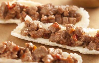 Fotografia em tons de marrom em uma bancada de madeira clara e mini barquinhas feitas com tapioca recheadas com picadinho de carne. Fotografia em tons de marrom em uma bancada de madeira clara e mini barquinhas feitas com tapioca recheadas com picadinho de carne.