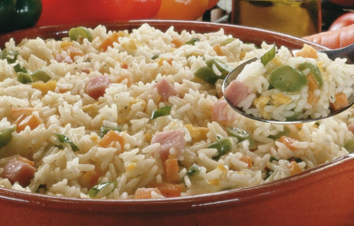 Fotografia em tons de argila e branco, com cumbuca de barro ao centro com arroz e legumes picados sobre guardanapo listrado em tons de argila, ao entorno pimentões, alho, cenoura, tomate-cereja, azeite, pedra vulcânica, tudo sobre bancada de pedra. Fotografia em tons de argila e branco, com cumbuca de barro ao centro com arroz e legumes picados sobre guardanapo listrado em tons de argila, ao entorno pimentões, alho, cenoura, tomate-cereja, azeite, pedra vulcânica, tudo sobre bancada de pedra.