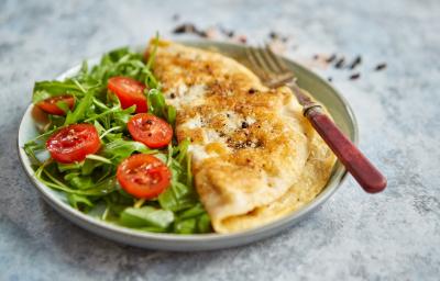 Foto da Receita de Omelete Baveuse. Observa-se um prato com a omelete dobrada no meio, servida com salada de rúcula e tomatinhos cerejas cortados ao meio. Foto da Receita de Omelete Baveuse. Observa-se um prato com a omelete dobrada no meio, servida com salada de rúcula e tomatinhos cerejas cortados ao meio.