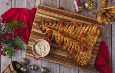 Foto vista de cima da receita de árvore folhada, decorada com tomates cereja, sobre um tecido vermelho com adereços natalinos ao redor. Foto vista de cima da receita de árvore folhada, decorada com tomates cereja, sobre um tecido vermelho com adereços natalinos ao redor.