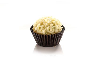 Fotografia em tons claros de um brigadeiro de erva cidreira e capim santo com raspas de chocolate branco em uma embalagem marrom. Fotografia em tons claros de um brigadeiro de erva cidreira e capim santo com raspas de chocolate branco em uma embalagem marrom.