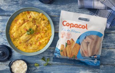 Foto da receita de Moqueca Fácil com Filé de Tilápia Copacol, vista de cima, servida em uma tigela azul clara, sobre uma bancada azul com alguns elementos de comida, um tecido e um pacote do produto Copacol Foto da receita de Moqueca Fácil com Filé de Tilápia Copacol, vista de cima, servida em uma tigela azul clara, sobre uma bancada azul com alguns elementos de comida, um tecido e um pacote do produto Copacol