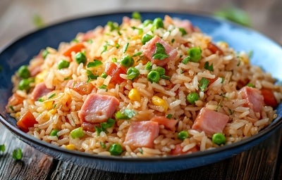 Em cima de uma mesa, prato redondo com porção de arroz com presunto cortado, ervilha, milho, decorado com cebolinha picada. Em cima de uma mesa, prato redondo com porção de arroz com presunto cortado, ervilha, milho, decorado com cebolinha picada.