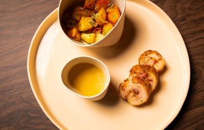 Foto da receita de BALOTINE DE FRANGO COM BATATAS LYONESE. Observa-se um prato visto de cima com o frango cortado em rodelas, servido com um molho ao lado e as batatas coradas.
