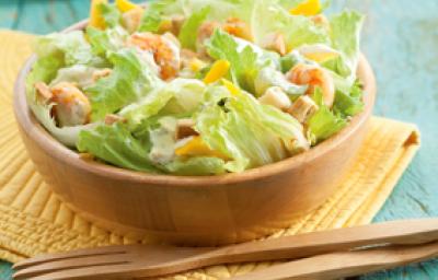 Fotografia em tons de azul, amarelo e marrom de uma bancada azul com um paninho amarelo, sobre ele um bowl de madeira com salada e uma colher e um garfo de madeira. Ao fundo pratos redondos brancos. Fotografia em tons de azul, amarelo e marrom de uma bancada azul com um paninho amarelo, sobre ele um bowl de madeira com salada e uma colher e um garfo de madeira. Ao fundo pratos redondos brancos.