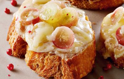 Fotografia em tons de amarelo em uma bancada de madeira escura com um prato branco raso e três bruschettas com queijo brie e uvas. Fotografia em tons de amarelo em uma bancada de madeira escura com um prato branco raso e três bruschettas com queijo brie e uvas.