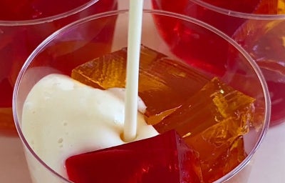 imagem mostra uma sobremesa de gelatina colorida cremosa, com cubos coloridos envoltos em creme branco.