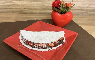 Fotografia em tons de vermelho e marrom com um prato vermelho ao centro. Em cima do prato existe uma receita de tapioca recheada de creme de amendoim e NESCAU Extra Cacau 60%