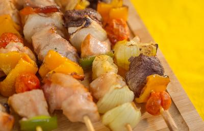 Imagem bem aproximada de uma tábua de madeira com cinco espetinhos sobre ela, alguns com frango, outros com carne e lombo. Eles também têm vegetais em tons verde, amarelo e vermelho. Imagem bem aproximada de uma tábua de madeira com cinco espetinhos sobre ela, alguns com frango, outros com carne e lombo. Eles também têm vegetais em tons verde, amarelo e vermelho.