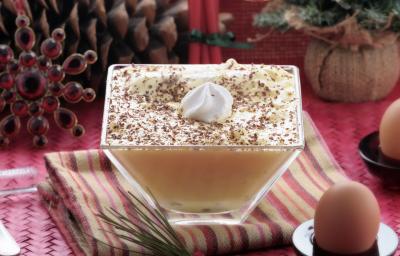 Fotografia de um flan de NESCAFÉ ao molho zabaione dentro de um recipiente quadrado de vidro fundo, com raspas de chocolate e chantilly por cima. A sobremesa está sobre um pano de mesa colorido.