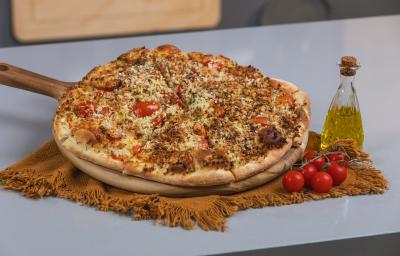 Foto da receita de massa básica de pizza, servida numa tábua de madeira com o sabor de pizza salgada. A tábua está ao lado de um galeteiro de azeite e alguns tomates.