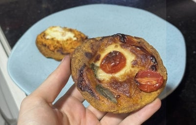 Fotografia de uma mão segurando uma mini pizza com massa de abóbora. No funo tem um prato raso azul com outra mini pizza.
