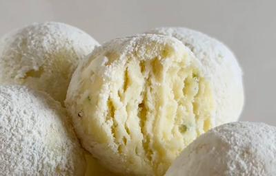 Fotografia de vários bombons de limão passados no leite em pó. O bombom do centro está aberto na metade, mostrando a textura e as raspas de limão. Fotografia de vários bombons de limão passados no leite em pó. O bombom do centro está aberto na metade, mostrando a textura e as raspas de limão.