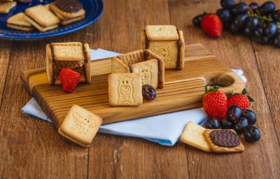 Foto de um balcão de madeira com uma pequena tábua com biscoitos em cima, alguns abertos, alguns morangos e uvas e um tecido em tom azul claro.