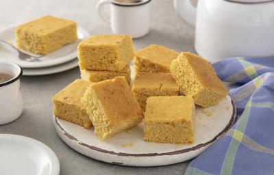 Foto da receita de Bolo de fubá sem glúten. Observa-se um prato de cerâmica com fatias quadradas do bolo e, ao lado esquerdo, uma xícara branca de café. Foto da receita de Bolo de fubá sem glúten. Observa-se um prato de cerâmica com fatias quadradas do bolo e, ao lado esquerdo, uma xícara branca de café.