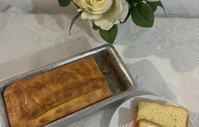 Fotografia vista de cima de um pão dentro de uma forma pequena retangular de alumínio ao lado de um prato pequeno raso com uma fatia do pão. Fotografia vista de cima de um pão dentro de uma forma pequena retangular de alumínio ao lado de um prato pequeno raso com uma fatia do pão.