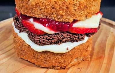 imagem mostra um bolo em formato de hambúrguer, com camadas de brigadeiro, geleia de morango, morangos e KitKat®.