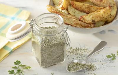Foto da receita de Sal de Ervas. Observa-se um pote de vidro hermético com o sal dentro e atrás, batatas assadas em um potinho Foto da receita de Sal de Ervas. Observa-se um pote de vidro hermético com o sal dentro e atrás, batatas assadas em um potinho