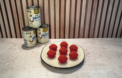 Fotografia em tons de bege em uma bancada, Leite Moça ao fundo e um prato ao centro com brigadeiros de frutas vermelhas.