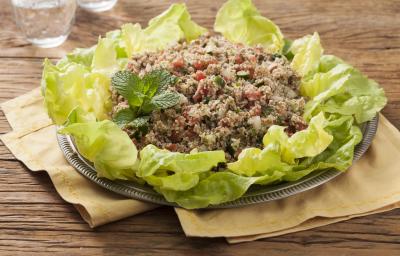 Em uma mesa de madeira contém panos em tons pardo abaixo de um recipiente que comporta a salada para quibe.