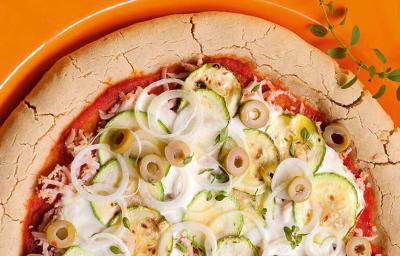 em um prato redondo laranja contém uma pizza com abobrinha, peito de peru e requeijão.