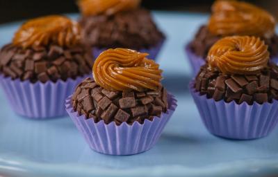 Fotografia de cinco unidades de forminhas azuis com brigadeiro de pão de mel, com doce de leite por cima de cada unidade. Os brigadeiros estão sobre um apoio decorativo de cor azul. Fotografia de cinco unidades de forminhas azuis com brigadeiro de pão de mel, com doce de leite por cima de cada unidade. Os brigadeiros estão sobre um apoio decorativo de cor azul.