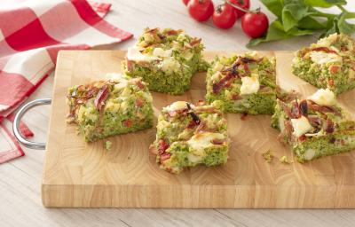 Fotografia em tons de verde e vermelho, ao centro uma tábua de madeira com 6 fatias da torta de espinafre, ao fundo um pano quadriculado vermelho e branco. Fotografia em tons de verde e vermelho, ao centro uma tábua de madeira com 6 fatias da torta de espinafre, ao fundo um pano quadriculado vermelho e branco.