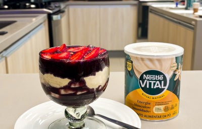 Fotografia em tons de amarelo e verde em uma bancada de cozinha com uma taça de vidro e o açaí dentro com camadas e morango em cima