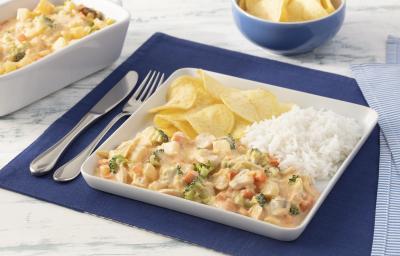 Fotografia em tons de azul em uma bancada de mármore branco com um jogo americano azul escuro, um prato quadrado branco grande com o strogonoff de legumes, arroz branco e batatas chips dentro dele. Ao fundo, um recipiente com mais strogonoff de legumes. Fotografia em tons de azul em uma bancada de mármore branco com um jogo americano azul escuro, um prato quadrado branco grande com o strogonoff de legumes, arroz branco e batatas chips dentro dele. Ao fundo, um recipiente com mais strogonoff de legumes.