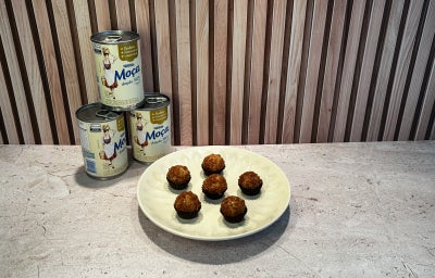 Fotografia em tons de bege em uma bancada, Leite Moça ao fundo e um prato redondo ao centro com brigadeiros.
