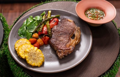 Bife de chorizo grelhado com legumes confitados, espiga de milho em rodelas e vinagrete ao lado