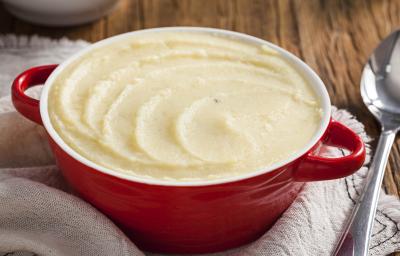 Foto de uma panela vermelha cheia de purê de batatas, acima de um pano bege e ao lado uma colher de servir prateada Foto de uma panela vermelha cheia de purê de batatas, acima de um pano bege e ao lado uma colher de servir prateada